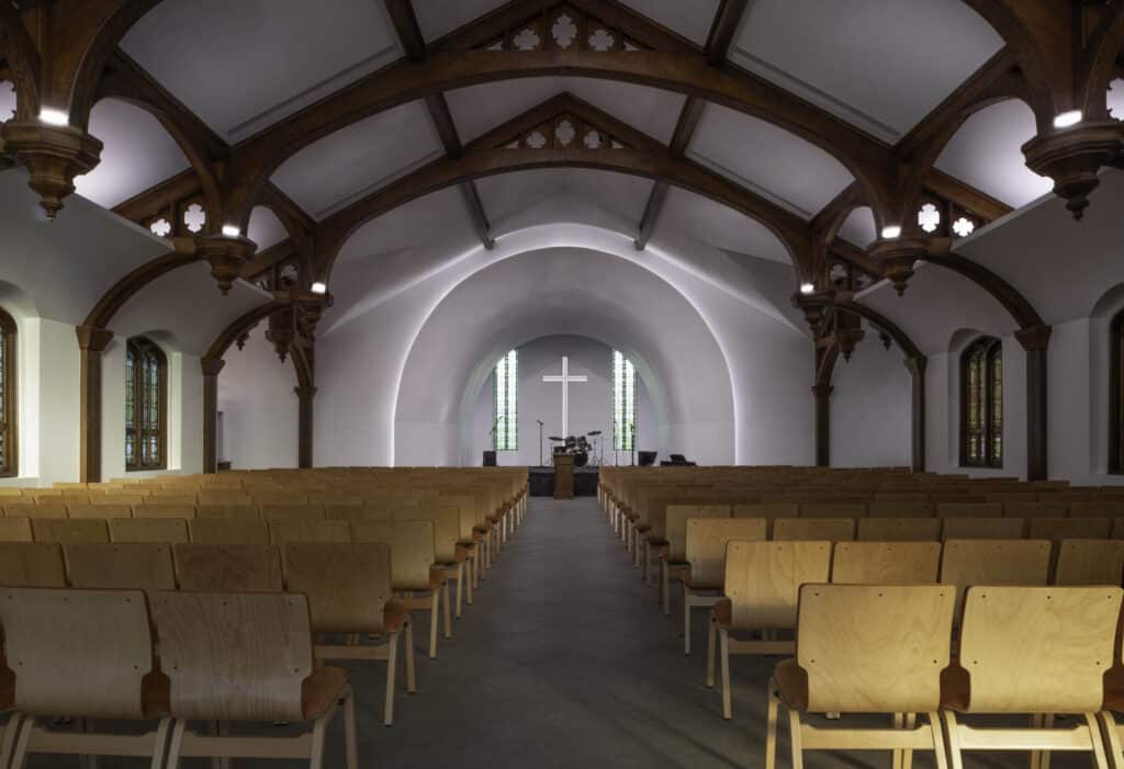 Wide view of the renovated Voorhees Chapel nave with wood seating and restored arches at University of Jamestown.