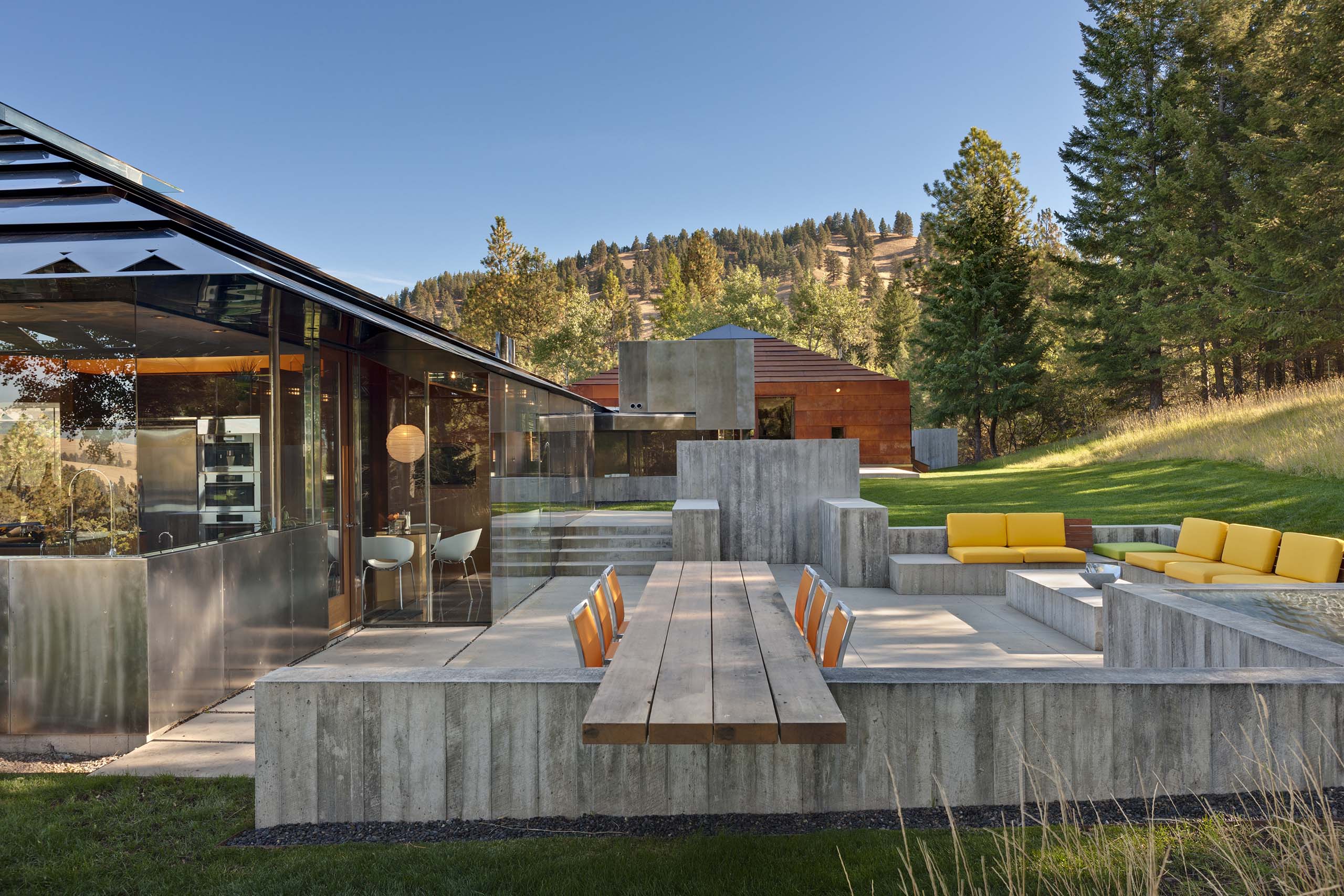 starwood-residence-outdoor-patio-concrete-dining-table-yellow-seating-mountain-view-eddie-jones-faia-jones-studio-missoula-montana.jpg Outdoor patio and dining terrace at Starwood Residence by Eddie Jones FAIA Jones Studio Inc Missoula Montana showing board-formed concrete dining table and benches yellow outdoor seating glass living pavilion and Montana mountain valley view